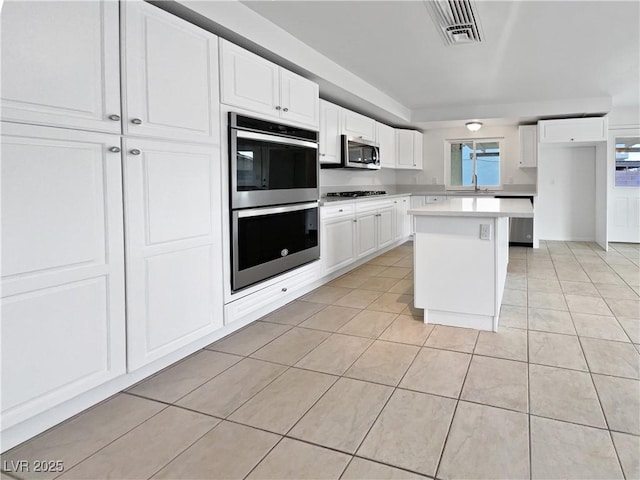 kitchen with light tile patterned flooring, appliances with stainless steel finishes, a kitchen island, and white cabinets