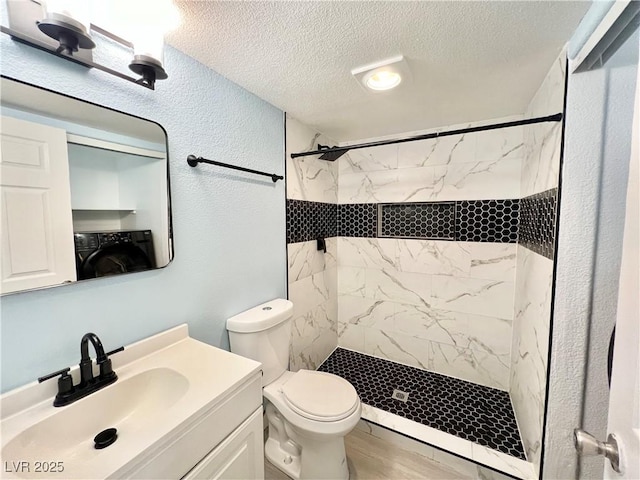 bathroom with a tile shower, washer / clothes dryer, vanity, toilet, and a textured ceiling