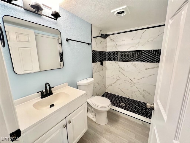 bathroom with a tile shower, vanity, wood-type flooring, a textured ceiling, and toilet