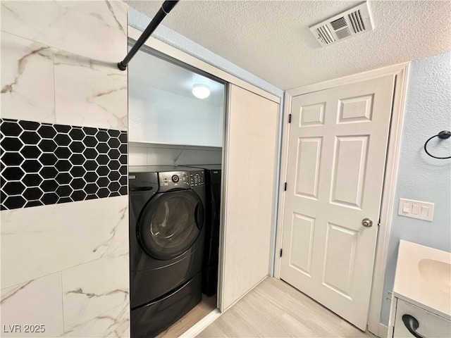 laundry area featuring washer / clothes dryer, sink, a textured ceiling, and light hardwood / wood-style flooring