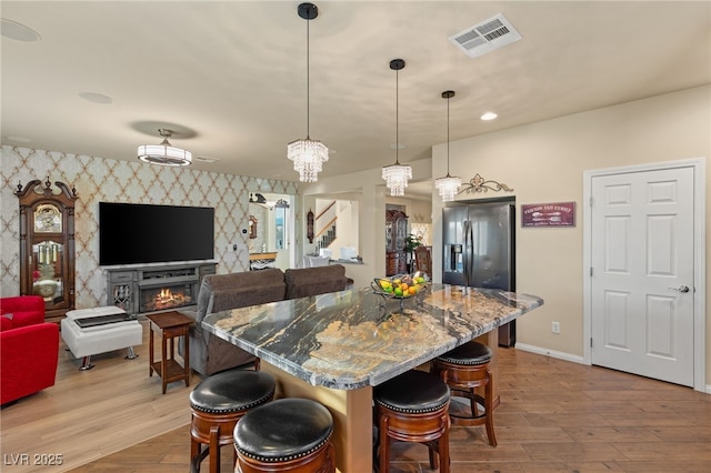 kitchen with visible vents, a kitchen breakfast bar, stainless steel fridge, wallpapered walls, and an accent wall