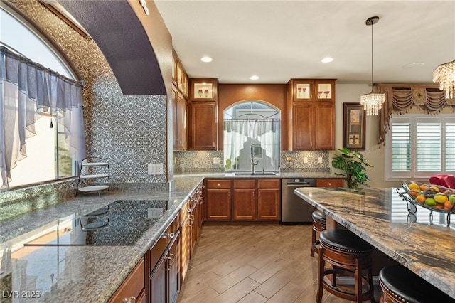 kitchen featuring brown cabinets, a sink, stainless steel dishwasher, an inviting chandelier, and a healthy amount of sunlight