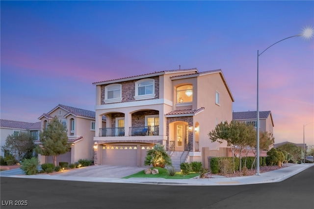 mediterranean / spanish home featuring stucco siding, driveway, a tile roof, stone siding, and an attached garage