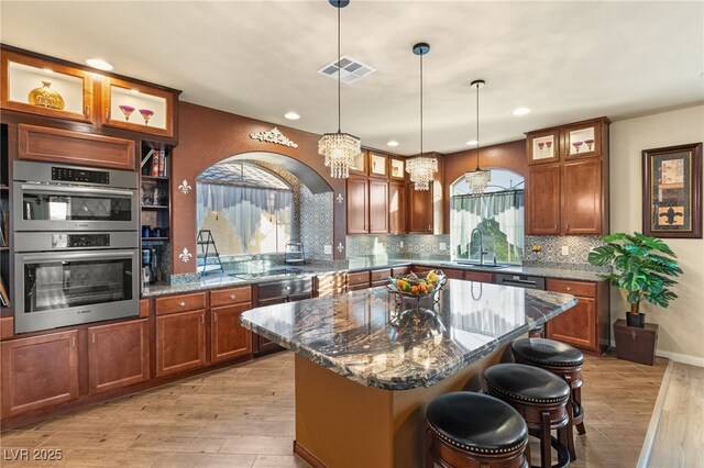 kitchen featuring a breakfast bar, hanging light fixtures, dark stone countertops, double oven, and a kitchen island