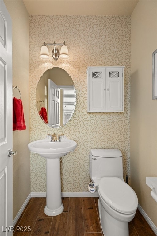 bathroom featuring baseboards, toilet, wood finished floors, and wallpapered walls