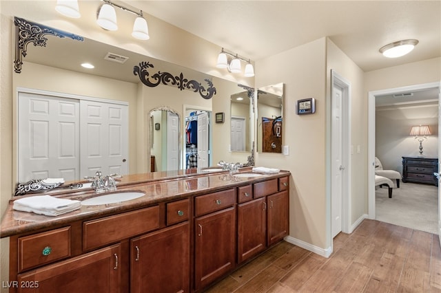 ensuite bathroom with visible vents, baseboards, double vanity, wood finished floors, and a sink