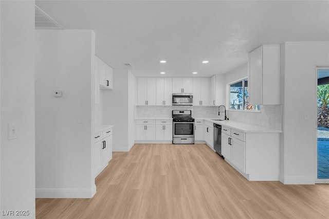 kitchen with appliances with stainless steel finishes, sink, white cabinets, and light wood-type flooring