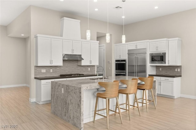 kitchen featuring sink, white cabinetry, built in appliances, decorative light fixtures, and an island with sink