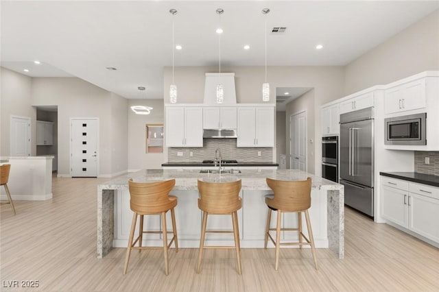 kitchen with built in appliances, hanging light fixtures, a large island, and dark stone countertops