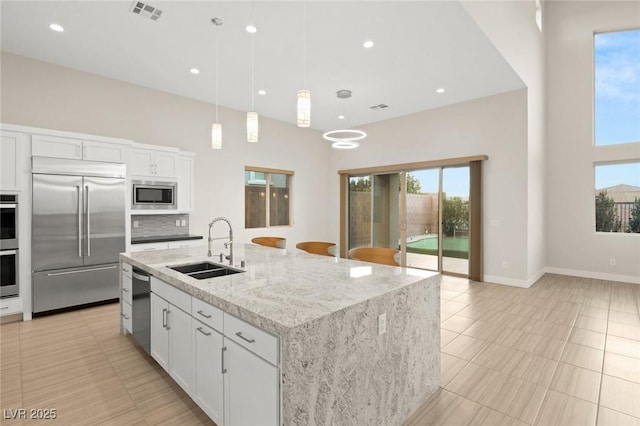 kitchen featuring sink, built in appliances, decorative light fixtures, an island with sink, and white cabinets