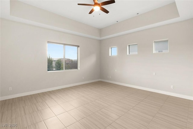 empty room with ceiling fan, a tray ceiling, and light tile patterned floors