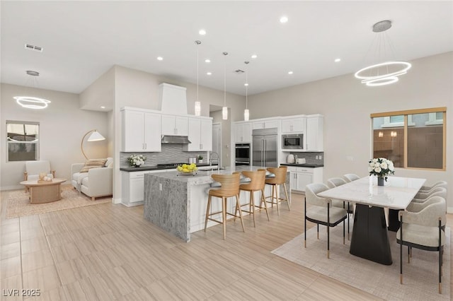 kitchen with built in appliances, white cabinetry, pendant lighting, and an island with sink