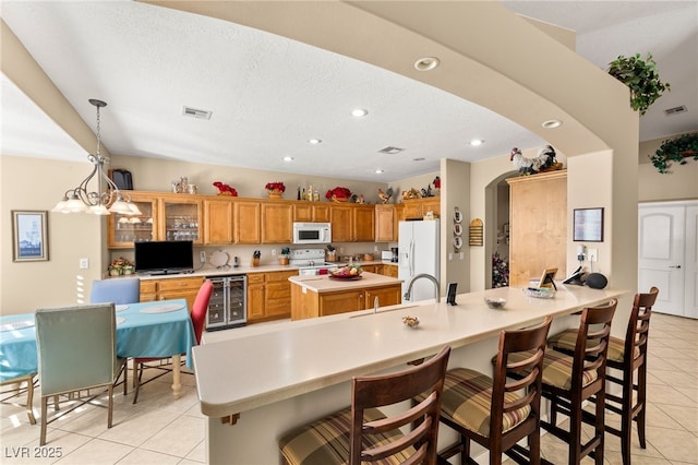 kitchen featuring wine cooler, light tile patterned flooring, a kitchen bar, kitchen peninsula, and white appliances