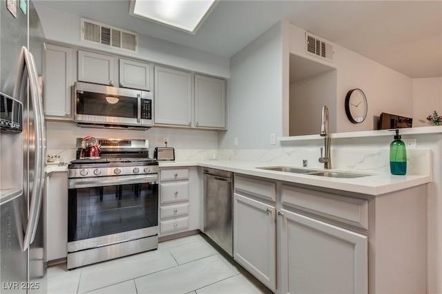 kitchen featuring appliances with stainless steel finishes, sink, gray cabinetry, light tile patterned floors, and light stone counters