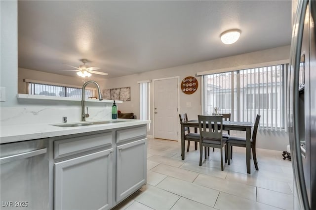 kitchen featuring sink, light tile patterned floors, ceiling fan, appliances with stainless steel finishes, and light stone counters