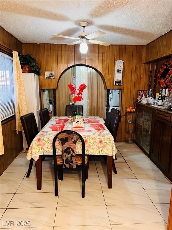 dining area with ceiling fan, a textured ceiling, and wood walls