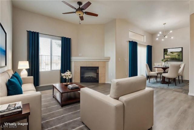 living room featuring a tiled fireplace, ceiling fan with notable chandelier, and hardwood / wood-style floors