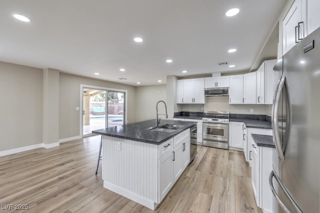 kitchen with sink, a kitchen island with sink, white cabinetry, stainless steel appliances, and light hardwood / wood-style floors