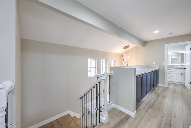 corridor with sink, lofted ceiling with beams, and light wood-type flooring