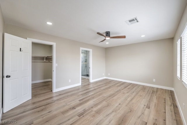 unfurnished bedroom featuring ceiling fan, ensuite bathroom, a walk in closet, a closet, and light wood-type flooring