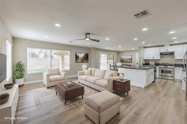 living room with a healthy amount of sunlight, sink, and light wood-type flooring