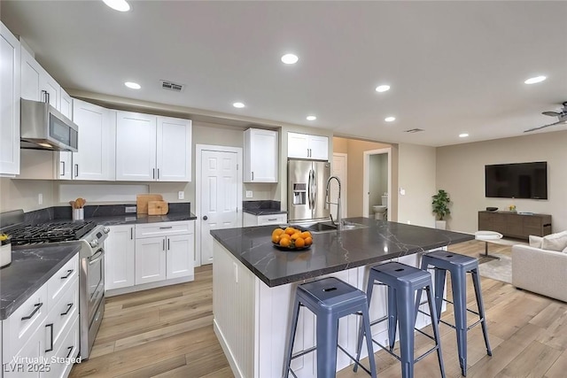 kitchen featuring a breakfast bar, white cabinetry, a center island with sink, light hardwood / wood-style flooring, and stainless steel appliances