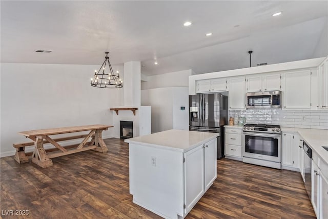 kitchen with appliances with stainless steel finishes, decorative light fixtures, white cabinetry, decorative backsplash, and a center island