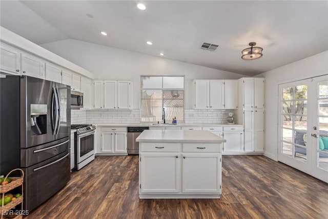 kitchen featuring appliances with stainless steel finishes, tasteful backsplash, white cabinetry, lofted ceiling, and french doors