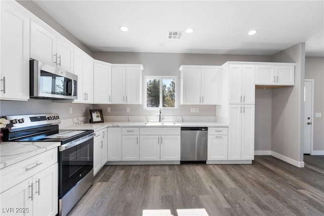 kitchen featuring sink, appliances with stainless steel finishes, light stone counters, wood-type flooring, and white cabinets