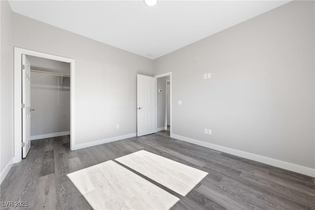 unfurnished bedroom featuring a spacious closet, dark wood-type flooring, and a closet