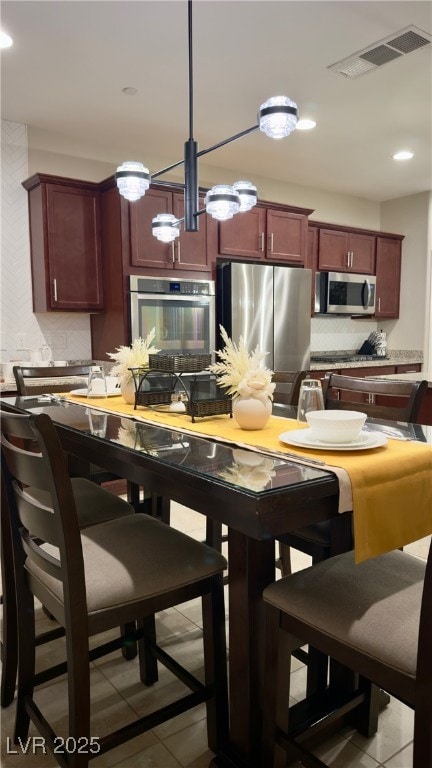 kitchen featuring tasteful backsplash, appliances with stainless steel finishes, decorative light fixtures, and light tile patterned floors