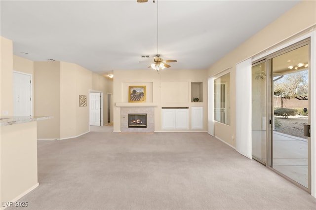 unfurnished living room featuring ceiling fan, a tiled fireplace, and light carpet