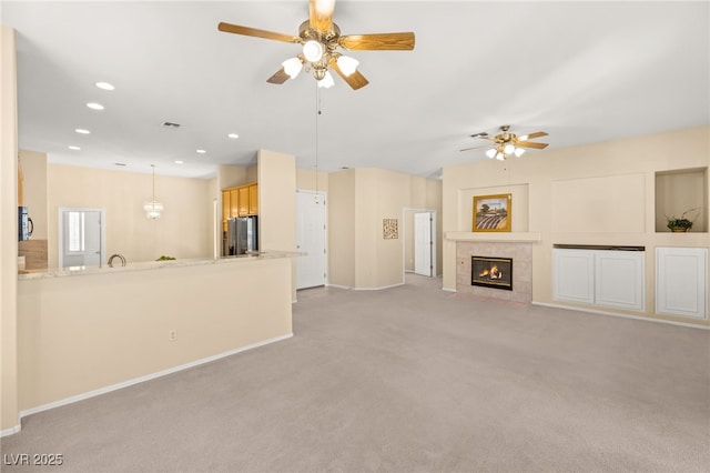 unfurnished living room featuring ceiling fan, a tiled fireplace, and light carpet