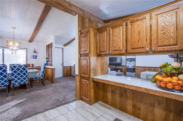 kitchen featuring tile countertops, wooden walls, hanging light fixtures, a notable chandelier, and light carpet