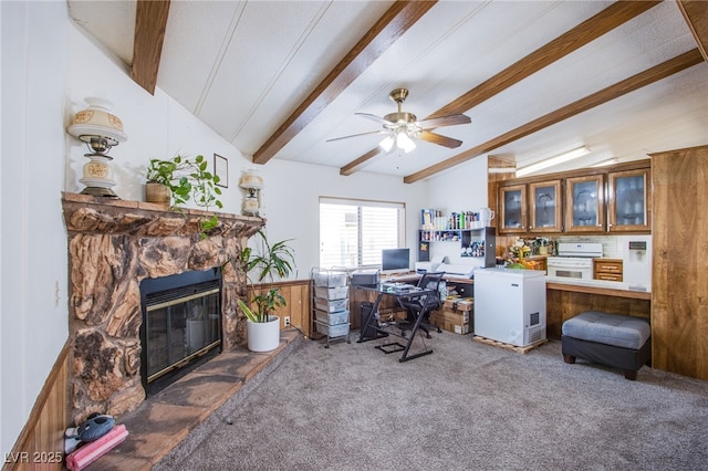 carpeted office space featuring ceiling fan, a stone fireplace, and lofted ceiling with beams