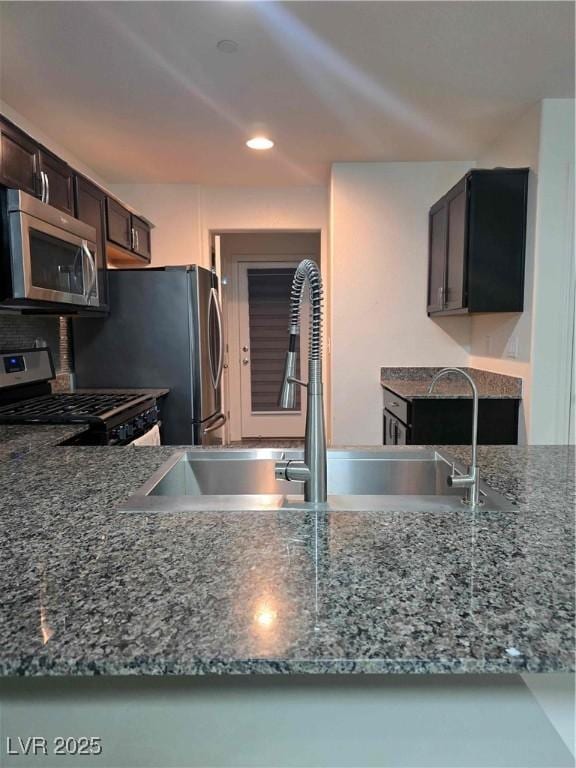 kitchen with appliances with stainless steel finishes, sink, dark brown cabinets, and stone counters