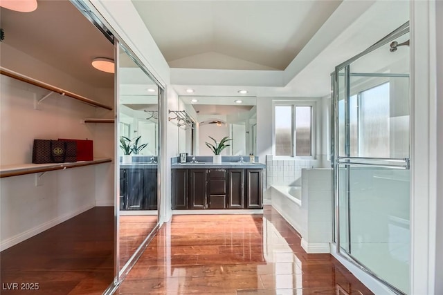 bathroom featuring hardwood / wood-style flooring, vanity, lofted ceiling, and tiled bath