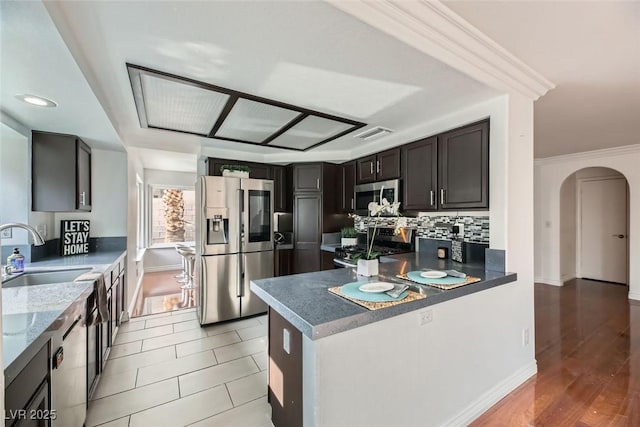 kitchen featuring sink, dark brown cabinets, ornamental molding, stainless steel appliances, and backsplash