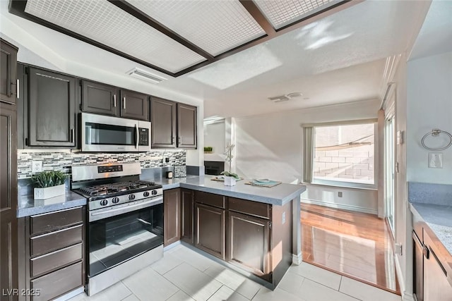 kitchen featuring dark brown cabinets, light tile patterned floors, kitchen peninsula, stainless steel appliances, and decorative backsplash