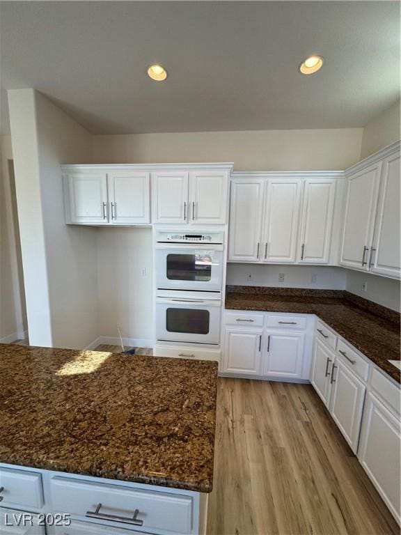 kitchen featuring light wood-type flooring, white cabinets, double oven, and dark stone counters