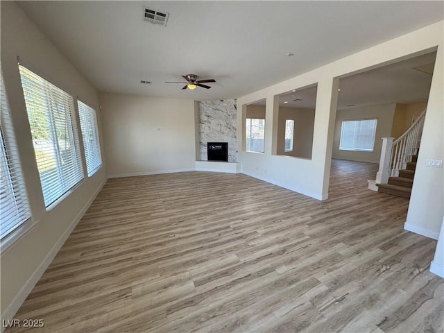 unfurnished living room featuring ceiling fan, plenty of natural light, a fireplace, and light wood-type flooring