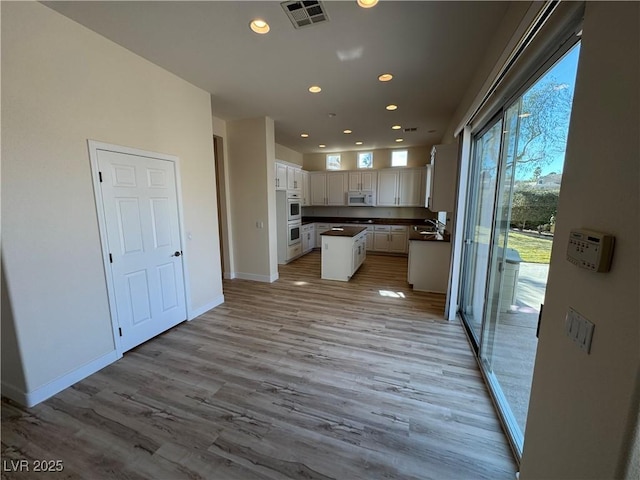 kitchen with double oven, white cabinetry, sink, a center island, and light wood-type flooring