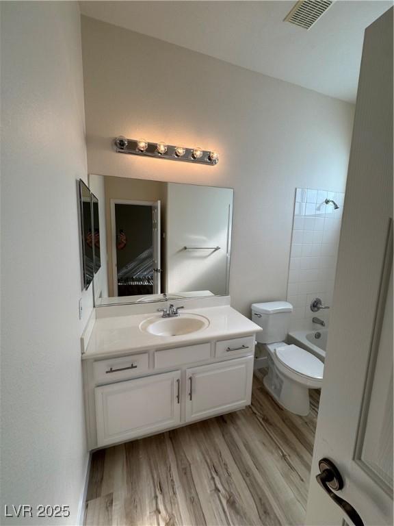 full bathroom with vanity, hardwood / wood-style floors, shower / bathtub combination, and toilet