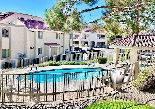 community pool with a patio area, fence, and a residential view