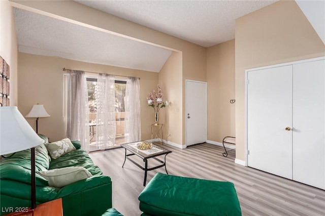 living area with vaulted ceiling, a textured ceiling, baseboards, and wood finished floors