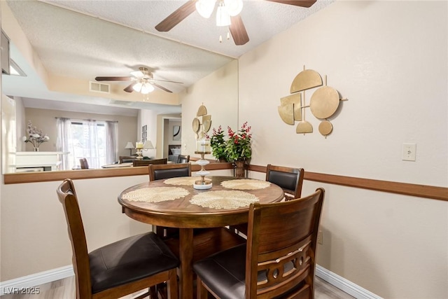 dining space with a textured ceiling, light wood finished floors, a fireplace, and visible vents