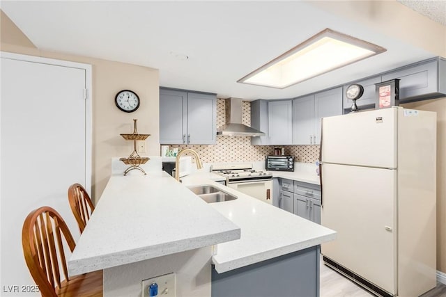 kitchen with sink, kitchen peninsula, white appliances, wall chimney range hood, and backsplash