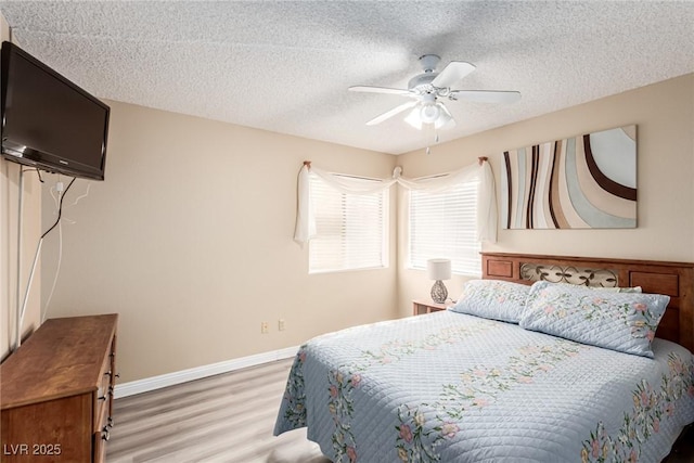 bedroom with a ceiling fan, light wood-type flooring, a textured ceiling, and baseboards