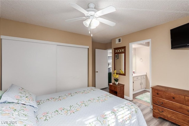 bedroom with light wood-style floors, a textured ceiling, visible vents, and a closet