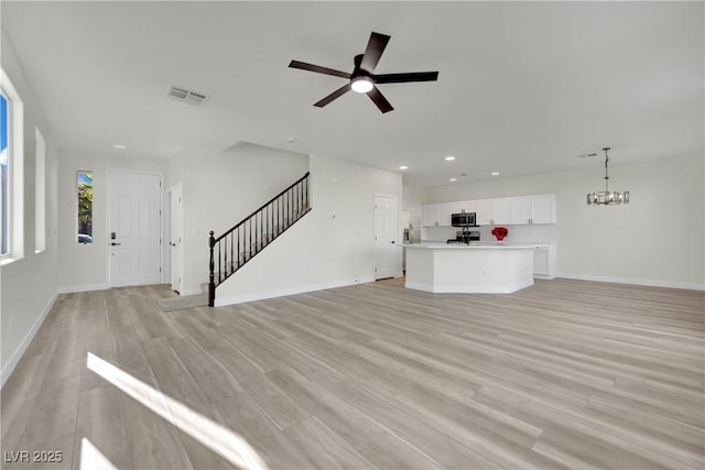 unfurnished living room with ceiling fan with notable chandelier and light hardwood / wood-style floors